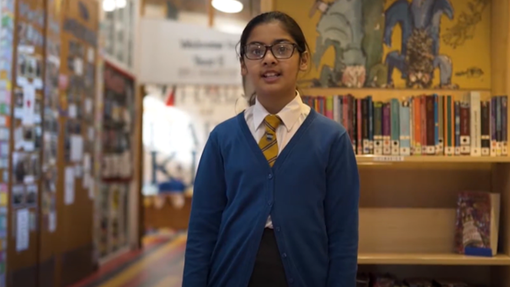 Female pupil talking to camera, standing in a school library