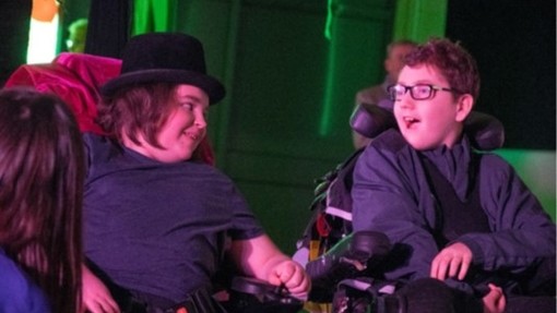 Two young boys in wheelchairs, performing on stage